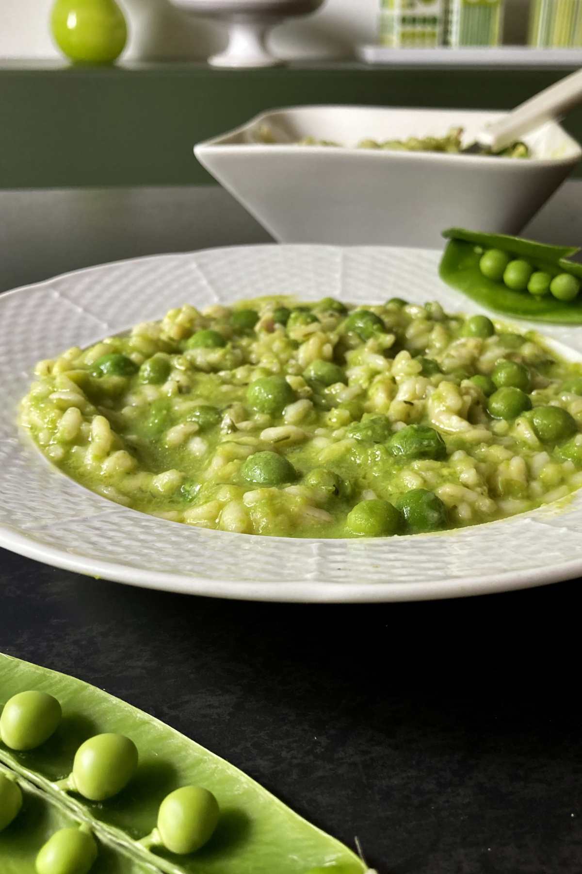 Risi e Bisi served in a white plate with fresh pea pods in the foreground