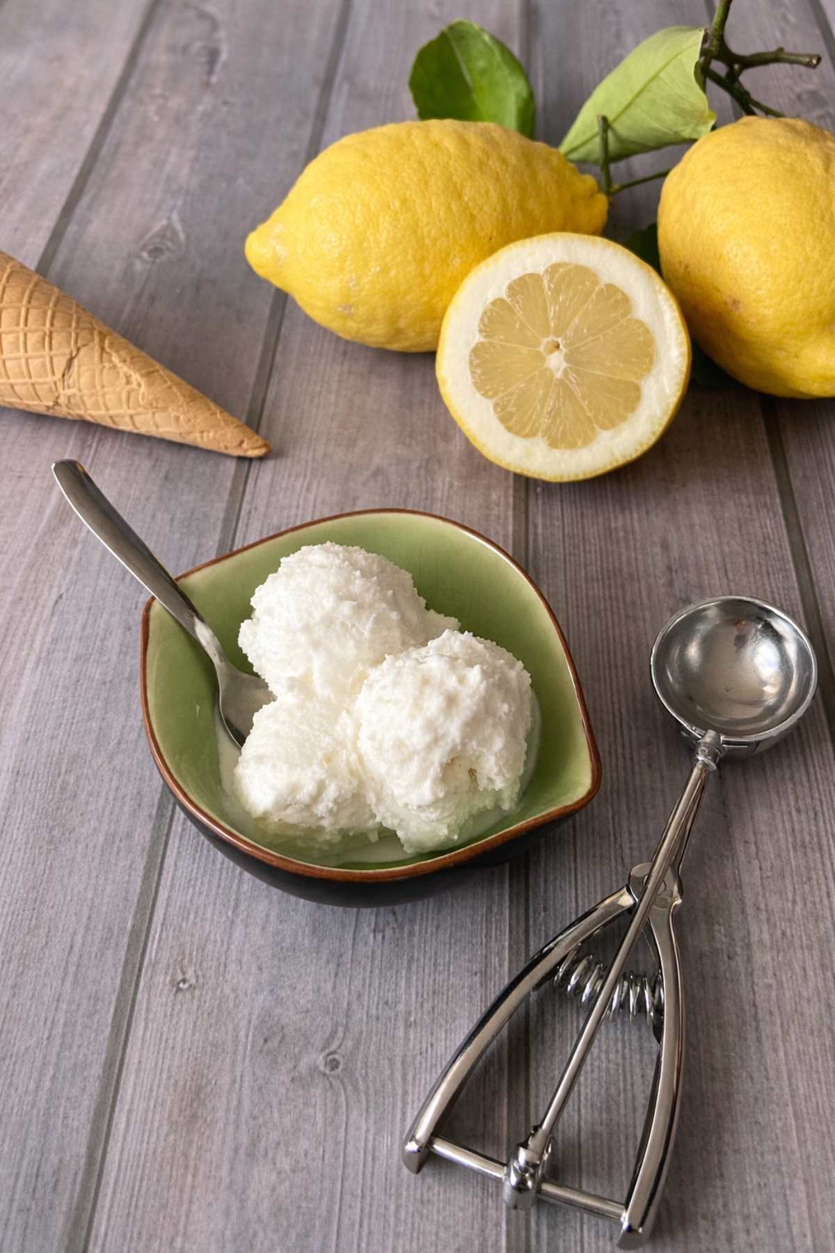 lemon gelato scoops with ice cream scoop and cone on wooden table