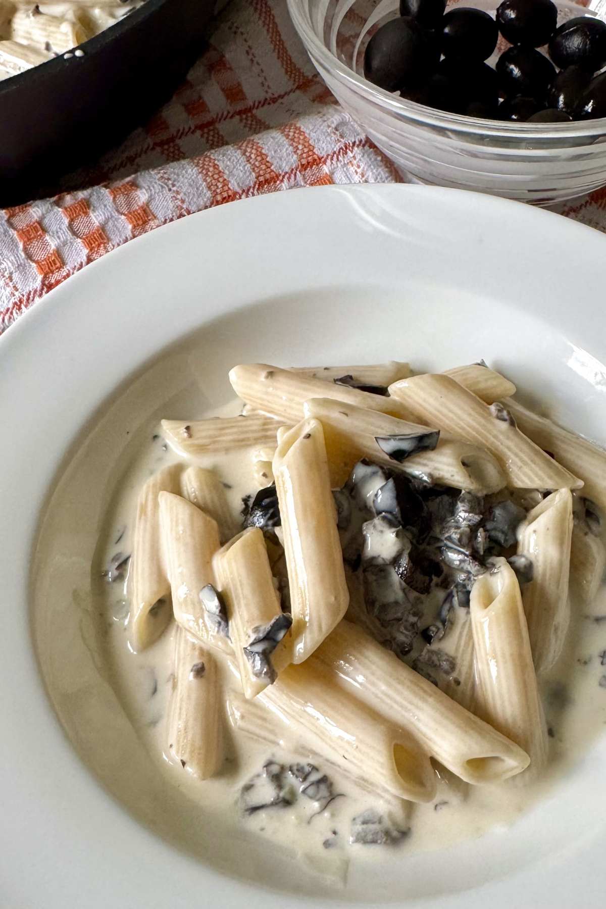 Pasta alla cenere with creamy gorgonzola sauce and black olives served on a white plate