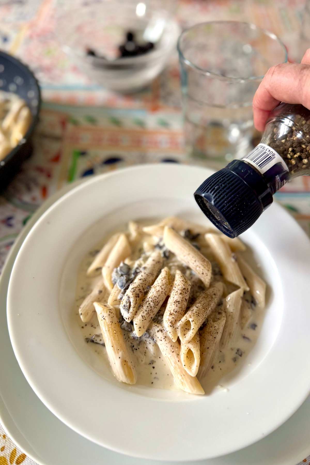 Creamy gorgonzola pasta with black olives being topped with freshly ground black pepper