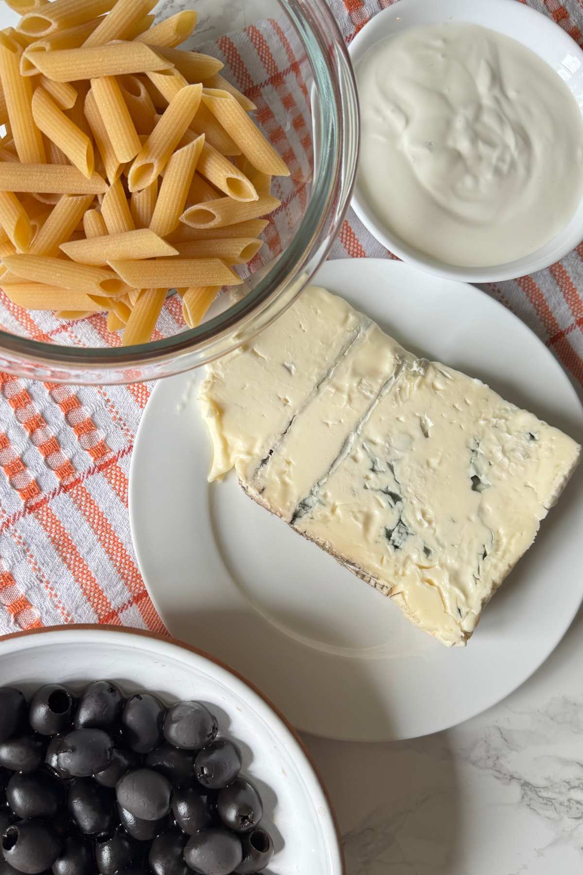 Ingredients for pasta alla cenere with penne pasta, gorgonzola cheese, black olives and cream
