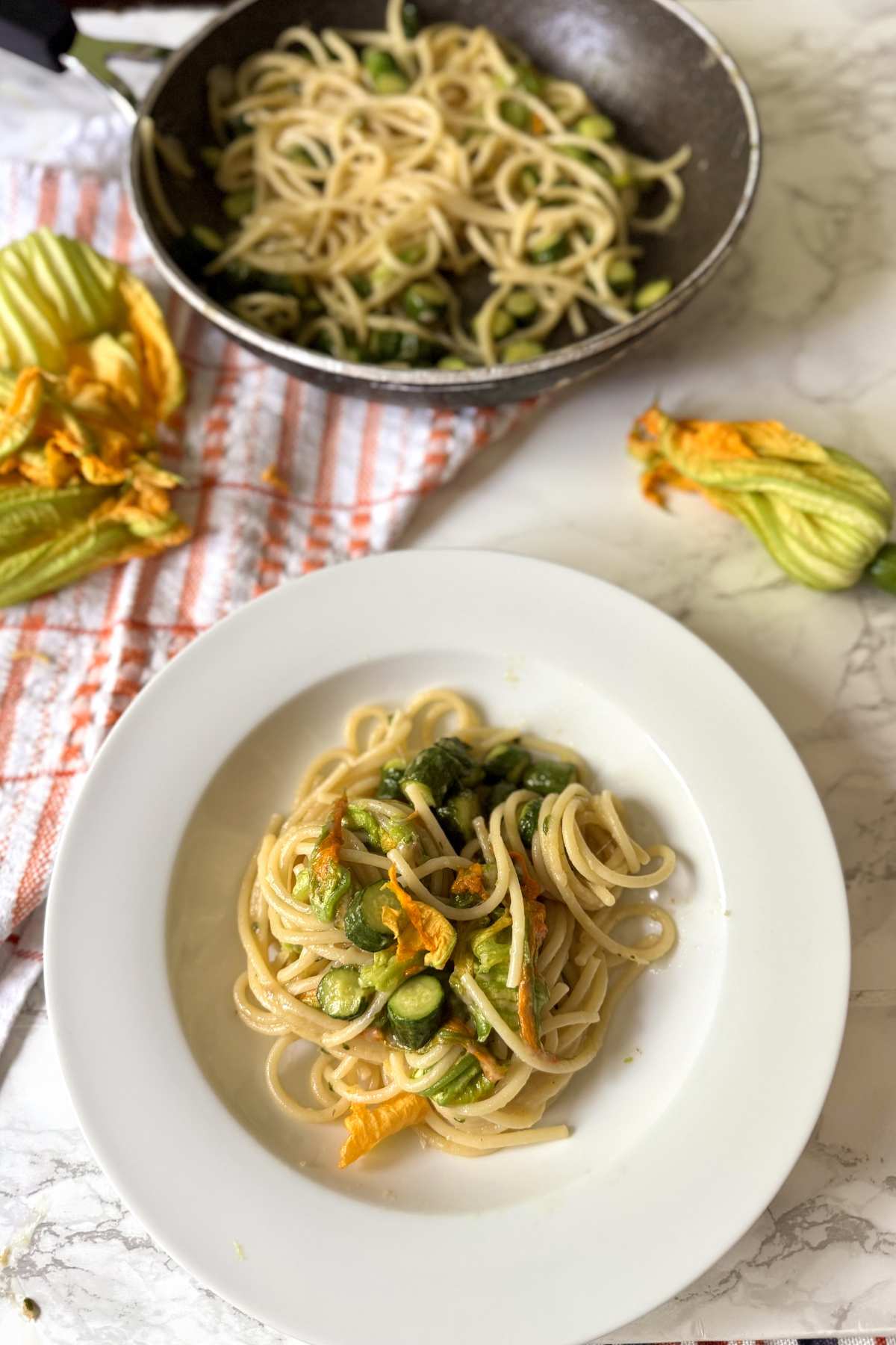 spaghetti with zucchini and zucchini flowers plated with skillet in background